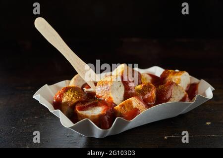 Gustosi pezzi di salsiccia di maiale fritta con ketchup di curry e bastone zero rifiuti in ciotola da asporto su sfondo nero Foto Stock