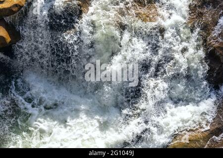 Primo piano struttura astratta sopra la vista del torrente del fiume e acqua fresca limpida che scorre attraverso le rocce di montagna in valle con schiuma e bolle su Foto Stock