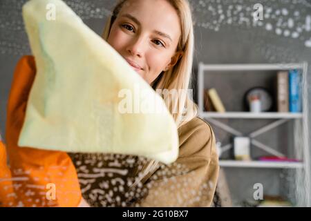 Donna felice che lava il vetro con straccio e prodotto per la pulizia a casa Foto Stock