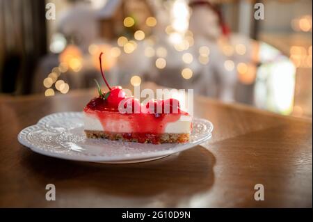 Fetta di cheesecake alla fragola con strato di biscotto, ciliegia e marmellata su piatto bianco al ristorante Foto Stock
