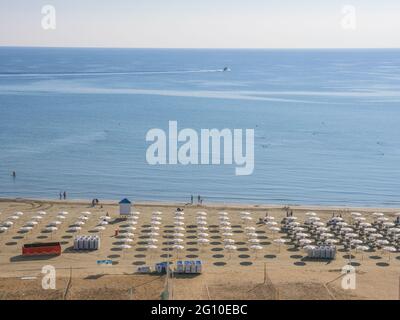 Vista dall'alto sulla spiaggia soleggiata e pittoresca con persone che prendono il sole, camminano e nuotano, ombrelloni, lettini, calmo mare blu mediterraneo Foto Stock