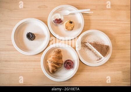 Vista dall'alto di Croissant, Banoffee, Scone, Canele su un piatto di carta su un tavolo di legno nel caffè Foto Stock