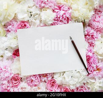 Foglio bianco di carta con spazio di copia e penna vintage giacente su sfondo floreale con peonie, rose e ortensie. Foto Stock