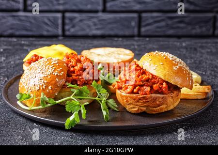 BBQ Sloppy Joe sandwich con french Fries su un piatto nero con un muro di mattoni sullo sfondo, primo piano, cucina americana Foto Stock