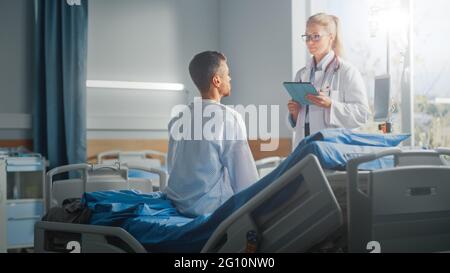 Hospital Ward: Seduta sul letto paziente maschio caucasico ascolta il medico femminile esperto che spiega i risultati del test, dà consigli, prescrive la medicina Foto Stock