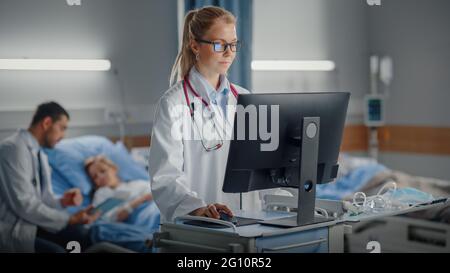 Hospital Ward: Medico femminile professionale o chirurgo utilizza un computer medico. In background ModernEquipment Clinic Doctor seduta e cura per Foto Stock