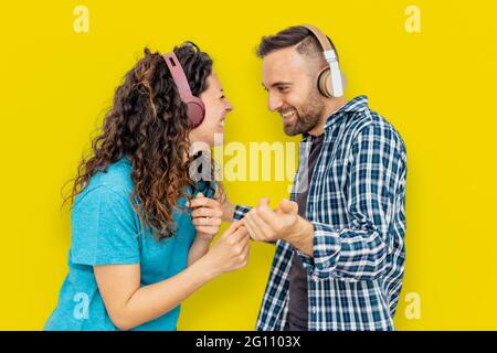 La coppia su sfondo giallo è divertirsi e ballare ascoltando musica con le cuffie Foto Stock