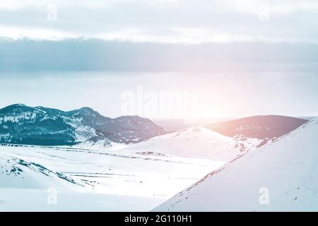 Vista di un paesaggio invernale con il sole che tramonta dietro le montagne sullo sfondo Foto Stock