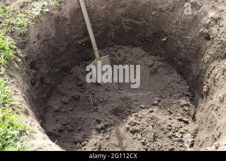 Fossa profonda nel terreno. Nella buca si trova una pala. Scavare un foro. Foto Stock