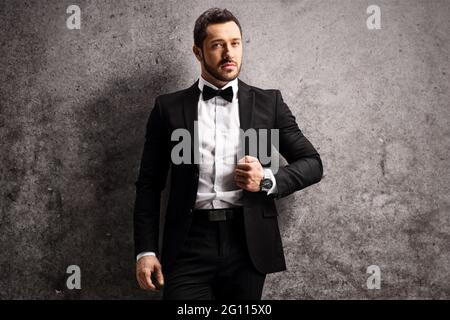 Giovane uomo in tuta nera e cravatta di prua appoggiata su una parete grigia arrugginita Foto Stock