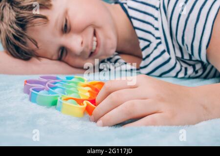 Ragazzo sorridente che gioca con il giocattolo iridato pop it fidget. Giocattolo sensoriale Fidget a bolla - giocattolo lavabile e riutilizzabile per alleviare lo stress. Giocattolo antistress per bambini Foto Stock