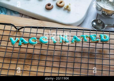 vaccinato scritto in biscotti che asciugano su una griglia di metallo su una tavola di legno con ghiaccio blu Foto Stock