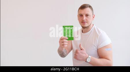 Uomo adulto che indossa una t-shirt con certificato internazionale di vaccinazione verde su sfondo bianco. Viaggiare passaporto immunitario, come prova vaccinato a. Foto Stock