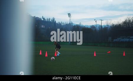 Giovane donna giocatore di calcio piazzando coni prima di calciare la palla sul campo di calcio. Foto Stock