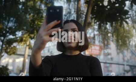 Giovane donna per strada effettua una videochiamata al telefono. Studente che fa chat video conferenza, relazioni remote, concetto di social distancing. Foto Stock