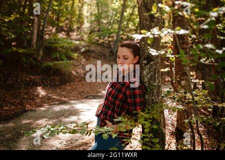 donna hipster viaggiatore in piedi da sola in autunno boschi in camicia a scacchi e jeans blu . Clima freddo, colori autunnali. Concetto Wanderlust. Foto Stock