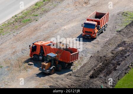 Un operatore su un trattore con una benna carica la terra in un camion. Chelyabinsk, Russia, 15 maggio 2021 Foto Stock