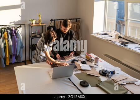 Il team di stilisti di abbigliamento sceglie il materiale per cucire la nuova collezione. I camerieri lavorano in studio di design Foto Stock