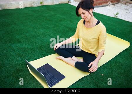 Una donna prende una lezione di yoga dal suo laptop all'aperto Foto Stock