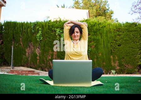 Una donna prende una lezione di yoga dal suo laptop all'aperto Foto Stock