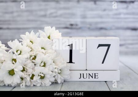 Blocchi di calendario in legno bianco con data 17 giugno e margherite bianche. Messa a fuoco selettiva con sfondo sfocato. Foto Stock