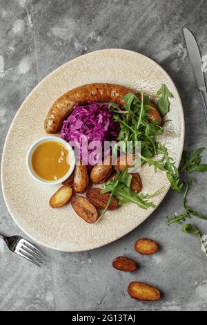 Salsicce di carne alla griglia e patate al forno con verdure su fondo grigio argilloso Foto Stock