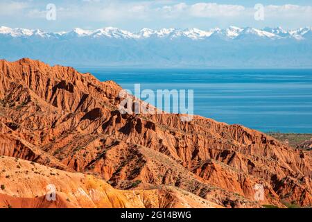 Formazioni rocciose rosse con il lago Issyk Kul sullo sfondo in Kaji Say, Kirghizistan. Foto Stock