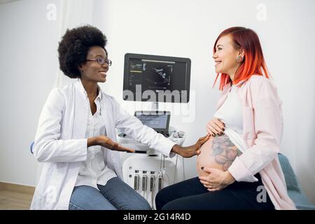 Ginecologia e ostetricia. Donna in gravidanza felice visita medico ecografo ginecologo in ospedale o clinica medica per il controllo della gravidanza. Il medico africano esamina la pancia incinta Foto Stock