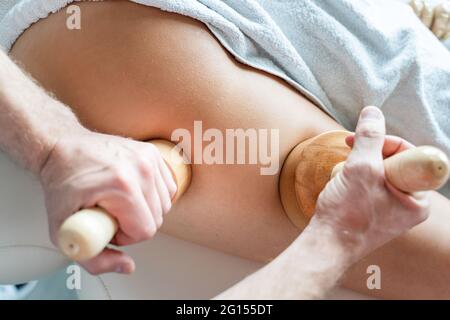 Primo piano sulla parte posteriore di donna sconosciuta che ha il massaggio di terapia di madero trattamento anticellulite da terapista professionista che tiene gli attrezzi di legno nelle mani in st Foto Stock