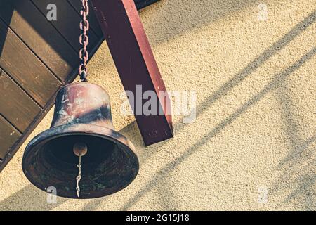 La grande campana della vecchia nave è appesa su una trave di legno come decorazione - la campana come decorazione su una catena. Foto Stock