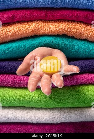 Donna che tiene il sapone tra gli asciugamani puliti. Sapone naturale giallo nella mano della donna su uno sfondo di asciugamani multicolore Foto Stock