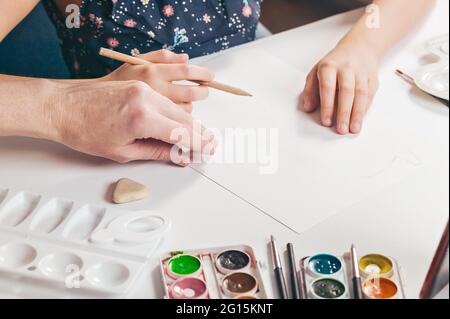 Belle donne e bambini mani nella cornice. La ragazza fa uno schizzo su un foglio bianco di carta e sua madre la aiuta. Mani nel telaio clos Foto Stock