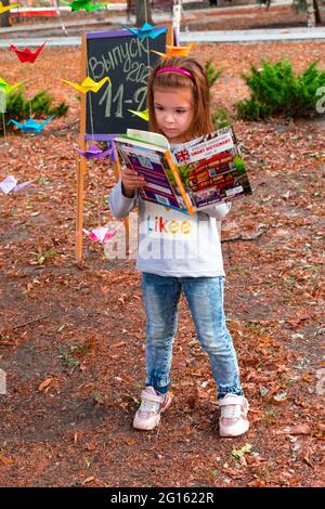 Lisichansk. Ucraina 10.04.2020. Edizione 2021 11 D. UNA studentessa di charme legge un libro di testo sullo sfondo di una lavagna in un parco autunnale. Indietro Foto Stock