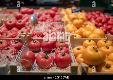 Pomodori maturi di varietà giallo rosso in una scatola di legno naturale ecologico al banco del mercato vegetale Foto Stock