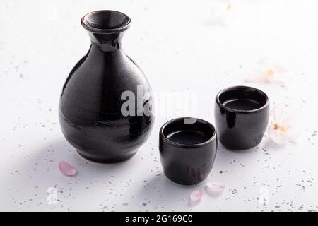 Sake forte con ciliegia fiorente. Abitudine giapponese di bere alcol. Ceramica nera su una pietra bianca. Foto Stock