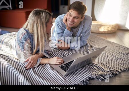 Una giovane coppia si diverse a letto guardando i contenuti del computer portatile in un'atmosfera rilassata a casa insieme. Coppia, amore, casa, rapporto Foto Stock