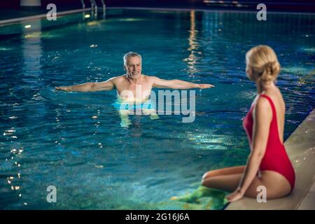 Bella donna bionda in costume da bagno rosso trascorrere il tempo in una piscina con il suo coniuge Foto Stock