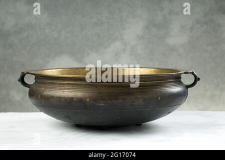 Urule o vaso di Ottone, un vuoto tradizionale sud indiano cucina vaso che è un pezzo antico posto su sfondo grigio textured. Foto Stock