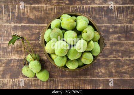 Mango grezzo disposto tradizionalmente in un vaso di ottone e mazzo di mango verde messo vicino su uno sfondo testurizzato di legno. Foto Stock