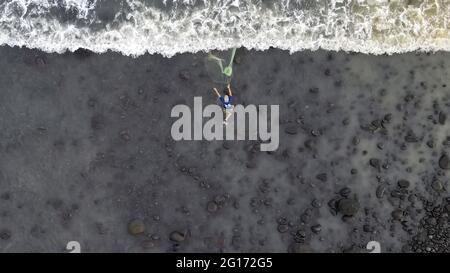 Tamanique, El Salvador. 04 giugno 2021. (NOTA DEI REDATTORI: Immagine presa con un drone) Vista aerea di un pescatore mentre lancia una rete nel mare per catturare il pesce mentre i surfisti catturano le onde di pratica. El Salvador ospita l'ISA World Surfing Games, dove i vincitori riceveranno i biglietti per le Olimpiadi di Tokyo. Credit: SOPA Images Limited/Alamy Live News Foto Stock