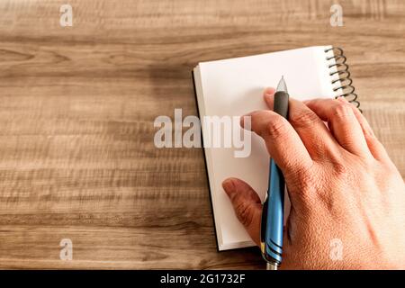 Vista dall'alto di una mano che tiene una penna su un notebook su una superficie di legno Foto Stock