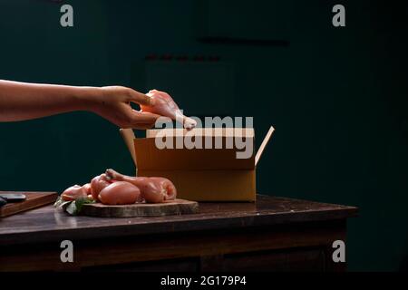 Tagli o parti grezzi di pollo senza pelle disposti su una base di legno tagliata a fette ed un lavoratore che impaccano il pollo crudo per la consegna che è messo su legno Foto Stock