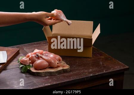 Tagli o parti grezzi di pollo senza pelle disposti su una base di legno tagliata a fette ed un lavoratore che impaccano il pollo crudo per la consegna che è messo su legno Foto Stock