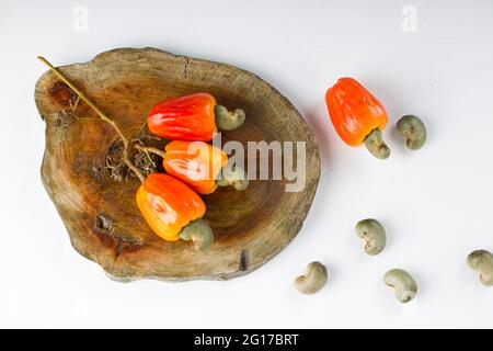 Mela di anacardi e semi di anacardi disposti su un pezzo di legno che è posto su sfondo bianco, fuoco selettivo. Foto Stock