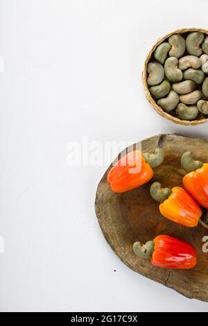 Mela di anacardi e semi di anacardi disposti su un pezzo di legno che è posto su sfondo bianco, fuoco selettivo e vista dall'alto. Foto Stock