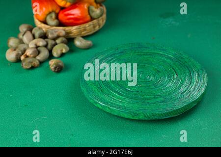 Mela di anacardi e semi di anacardi disposti su uno sfondo verde testurizzato con una base verde posizionata vicino, vista dall'alto. Foto Stock