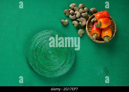 Mela di anacardi e semi di anacardi disposti su uno sfondo verde testurizzato con una base verde posizionata vicino, vista dall'alto. Foto Stock