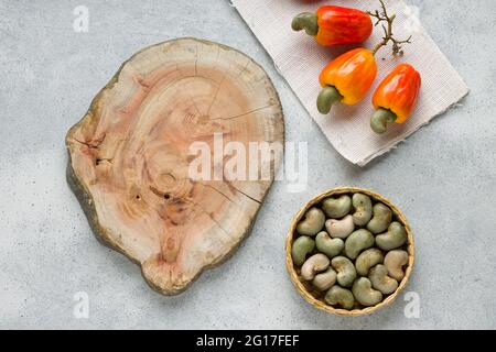 Mela di anacardi e semi di anacardi disposti su uno sfondo grigio testurizzato con un pezzo di legno posto vicino, vista dall'alto. Foto Stock