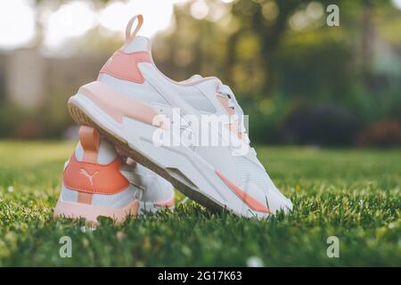 Minsk, Bielorussia, 23.05.2021: Sneakers PUMA da donna bianche con inserti corallini in piedi sull'erba nei raggi del sole Foto Stock