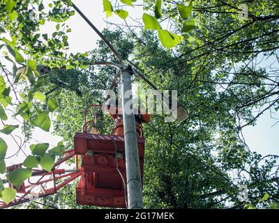 Un lavoratore municipale in apparecchiature di protezione esegue lavori pericolosi per eliminare un'interruzione nella rete elettrica. Un lavoratore ripara una lampada da strada da Foto Stock